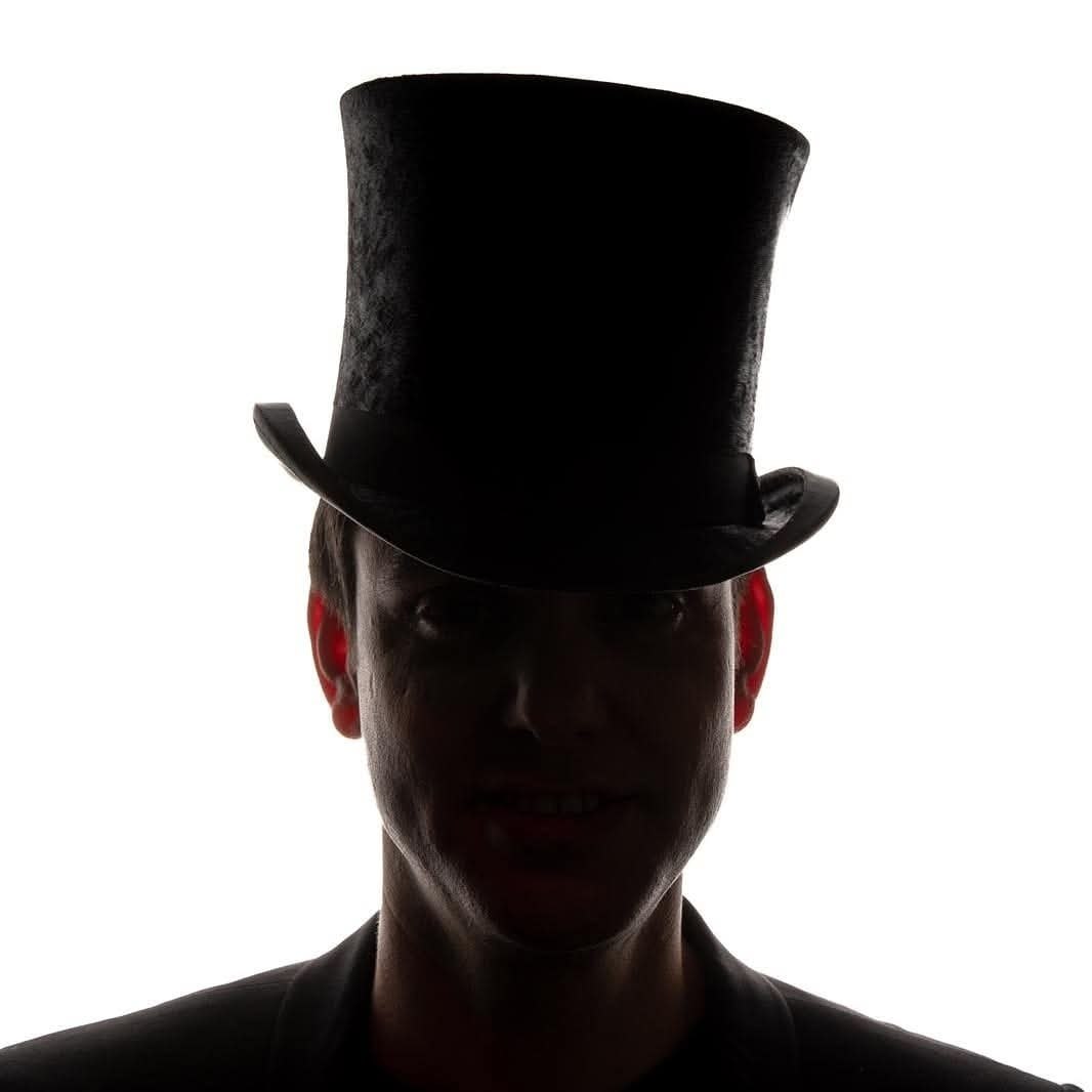 Dramatic portrait of Nickolai beneath his top hat, against a white background